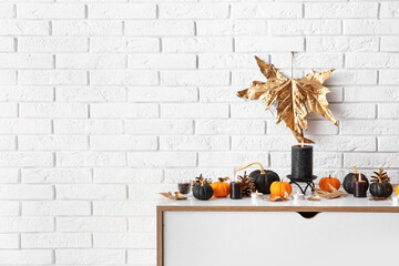 Chest of drawers with pumpkins, cones and candles near white brick wall