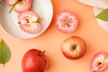 Plate with halves of sweet pink apple and leaves on orange background