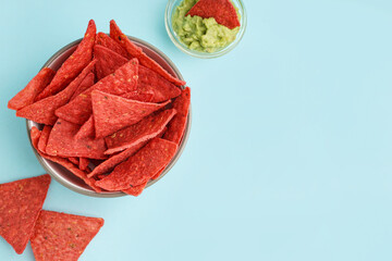 Bowl with red nachos and tasty guacamole on blue background