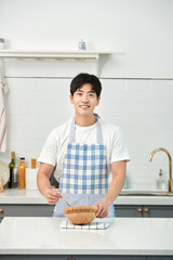 A young Asian man in the kitchen, wearing an apron, prepares a meal.