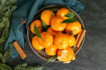 Plate of sweet mandarins with cinnamon, star anise and fir branches on black background