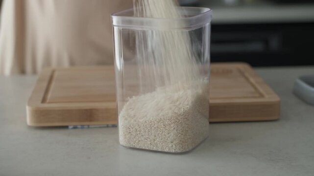 A detailed view of a Caucasian man pouring rice into a plastic container for storage on a clean kitchen countertop, showcasing organization and practicality in food management.