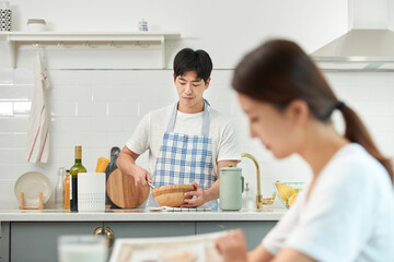The young husband is cooking in the kitchen while having a pleasant conversation with his wife