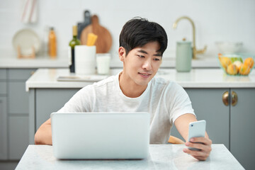 young, asian, man, white, t-shirt, kitchen, dining table, living room, laptop, smartphone, remote work, home office, casual attire, modern interior, healthy lifestyle, urban living, digital nomad, ind