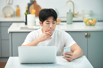 young, asian, man, white, t-shirt, kitchen, dining table, living room, laptop, smartphone, remote work, home office, casual attire, modern interior, healthy lifestyle, urban living, digital nomad, ind