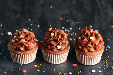Tasty chocolate cupcakes with sequins for Valentine's Day on grey grunge background