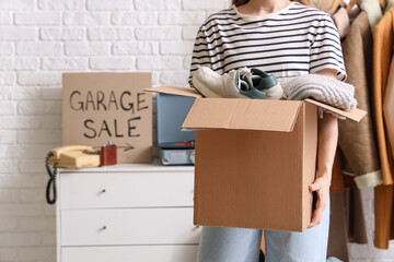 Woman holding box of unwanted stuff for garage sale in room © Pixel-Shot