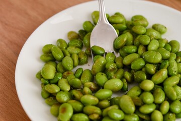 Green Edamame soy beans on the white plate with fork.