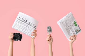Female hands with newspapers, microphone and photo camera on pink background