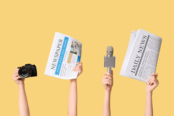Female hands with newspapers, microphone and photo camera on yellow background