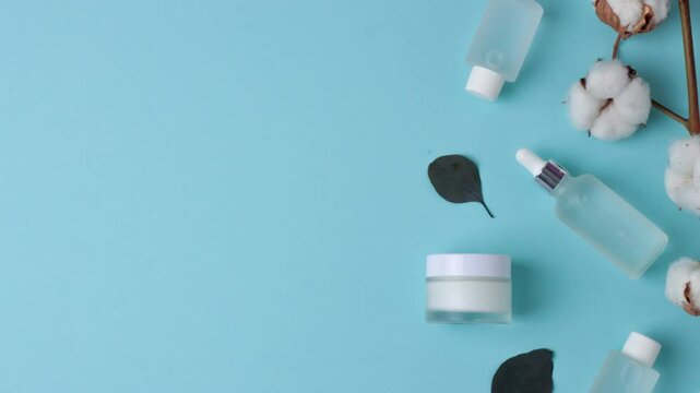 Cosmetic skin care products with flowers and eucalyptus on blue background. Flat lay, copy space