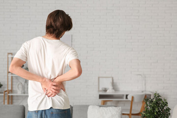 Handsome young man suffering from back pain at home