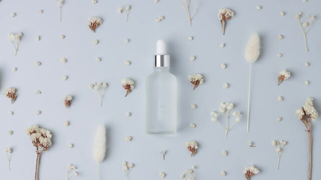 Cosmetic bottle with flowers on grey background. Flat lay