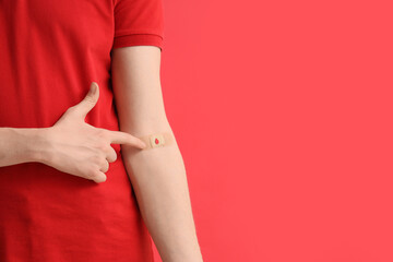 Male blood donor pointing at applied patch on red background, closeup
