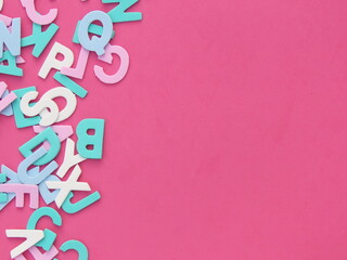 Multicolored eva foam letters scattered on pink background.
