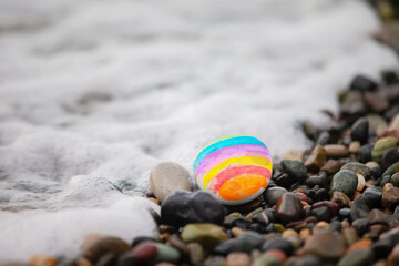 Obraz premium The sea stone on the shore is painted with rainbow stripes. The concept is bright and creative.