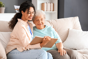 Young African-American female medical worker reading book with elderly woman in nursing home