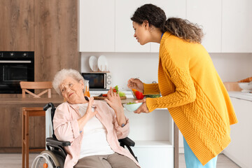 Elderly woman refusing food from young African-American female medical worker in nursing home