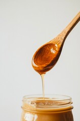 Close-up of honey dripping from wooden spoon into glass jar.