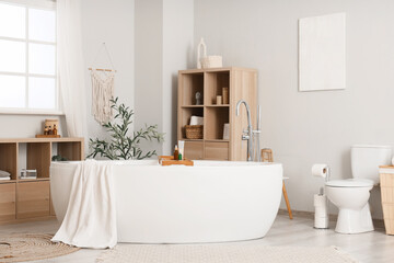 Bathtub with towel, toilet bowl and shelving units in interior of bathroom