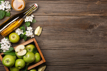 Ripe green apples in wooden box with branch of white flowers, glass and bottle of cider on a wooden table