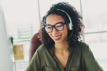 Young businesswoman wearing a headset and green shirt working in a modern office with natural...