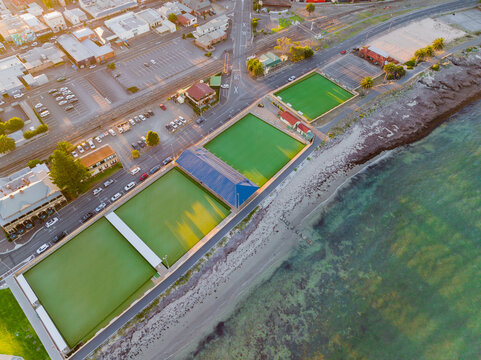 Aerial view of a row of bowling green sand tennis courts between city shopping centre and a beach