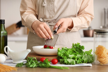 Woman grating garlic onto pasta at table in kitchen, closeup