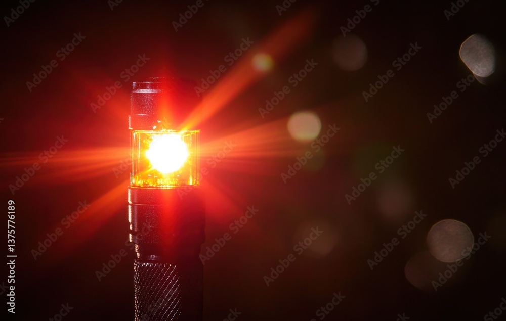 Aufkleber close-up of a flashlight with a yellow led light, dark background, red lens flare, bokeh effect, and