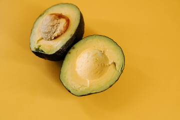 Fresh avocado cut in half revealing creamy interior on bright yellow background