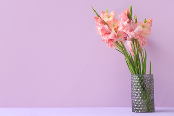 Glass vase with bouquet of beautiful gladiolus flowers on lilac background