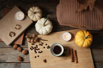 Cup of tasty pumpkin coffee with autumn decorations, books and warm sweater on brown wooden background