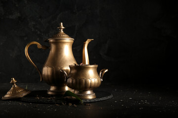 Tray with golden tea pot and bowl of dry tea on dark background