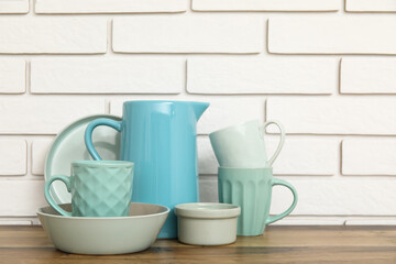Cups, bowls and jug on wooden table near white brick wall