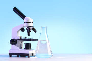 Modern microscope and laboratory flask with liquid on white table