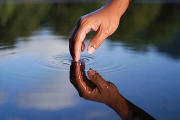 Fototapeta premium Female hand touching water creating ripples in calm lake