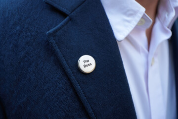 Close-up of person wearing blue coat with 'the boss' pin on lapel