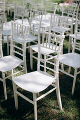 Rows of white Chiavari chairs stand on a green lawn in an outdoor event setting