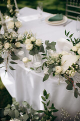 A white floral centerpiece with candles on a white tablecloth in an outdoor event setting