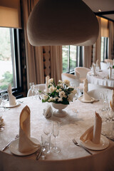 An elegant table setting for a wedding ceremony features white calla lilies, orchids, and freesia in a glass vase. Two candles in glass holders create a cozy, romantic atmosphere