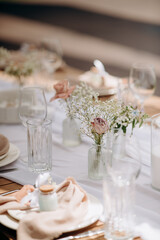 A delicate floral arrangement features white, pink, and red flowers (roses, orchids, carnations) in small, clear glass vases on a white tablecloth
