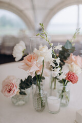 A delicate floral arrangement features white, pink, and red flowers (roses, orchids, carnations) in small, clear glass vases on a white tablecloth