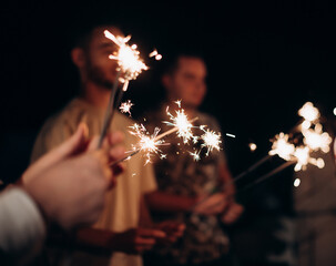 Close-up of people holding burning sparklers at night