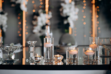 Floating candles in glass globes burning on a mirrored presidium of the newlyweds in a restaurant, creating an elegant and romantic atmosphere for the celebration