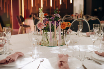 Tall candles and vibrant autumn flowers in the decor of the banquet table in the restaurant, creating a warm and festive atmosphere for the celebration