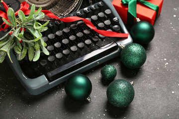 Vintage typewriter with Christmas balls, gift box and mistletoe branch on black background, closeup