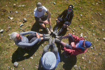 Group travelers sitting in circle with dusty trekking boots in center and chat during vacation.
