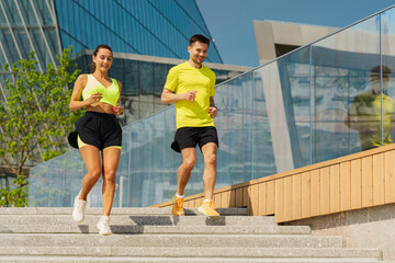 Couple Enjoying a Morning Jog Down City Steps in Vibrant Workout Attire Under a Clear Blue Sky