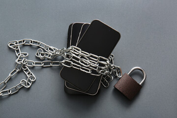 Different mobile phones with chain and padlock on dark background