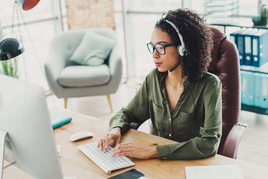 Young professional businesswoman working at her desk in a contemporary office wearing headphones